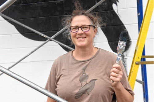 woman holding paint brush in front of mural